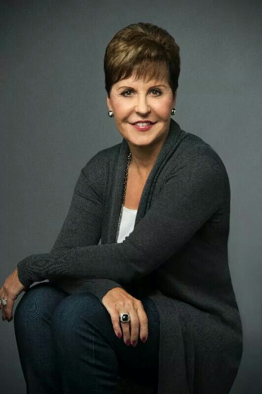 a woman sitting on top of a chair in front of a gray background wearing a black cardigan