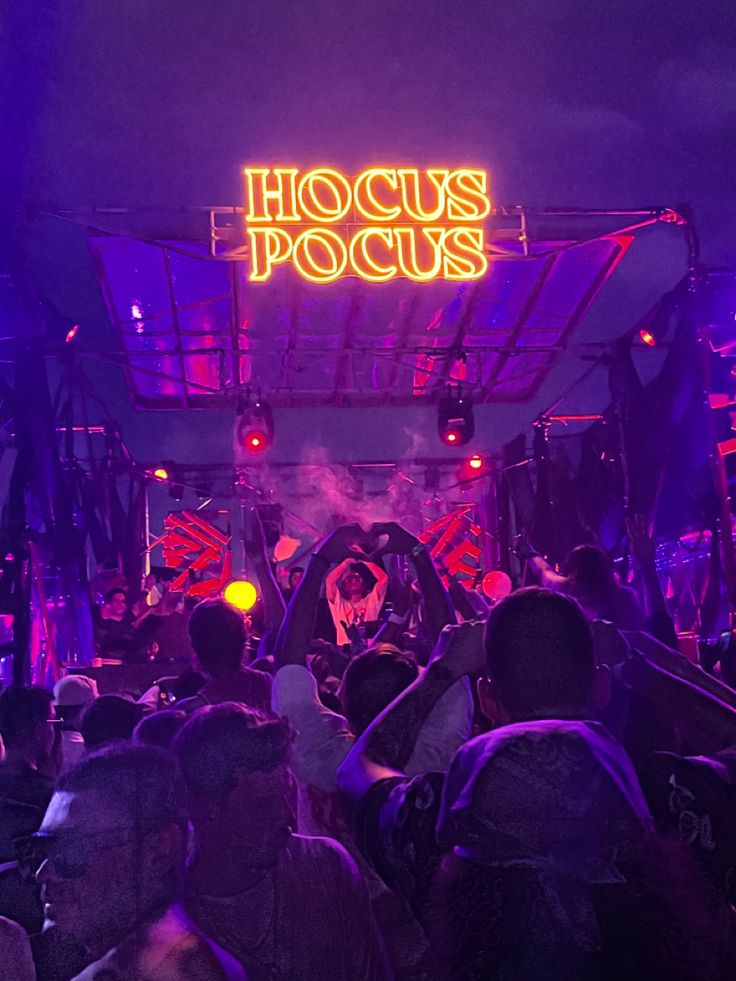 a large group of people standing in front of a neon sign that reads hoccus pocus