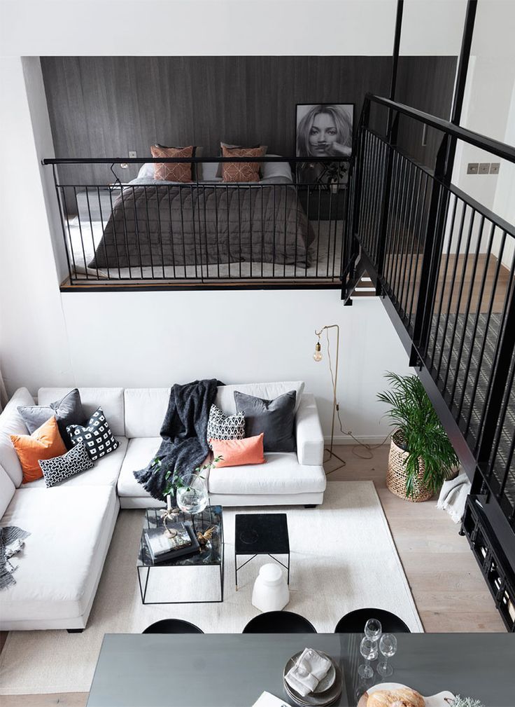 an overhead view of a living room with white couches and black railings on the second floor