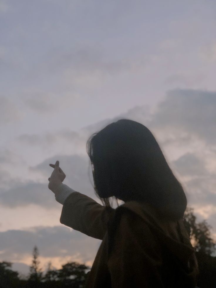 a woman standing in front of a cloudy sky holding a cell phone up to her ear