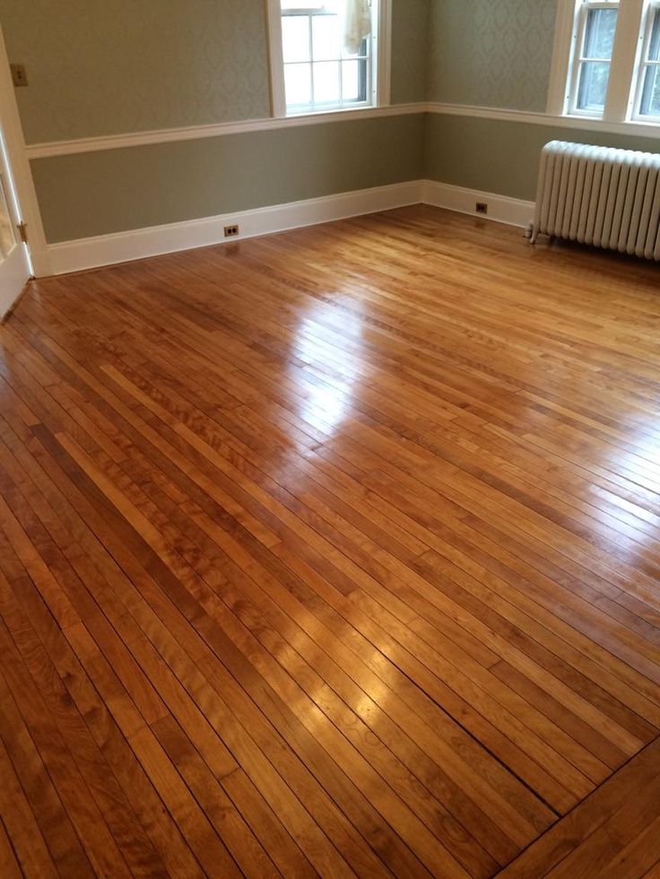 an empty room with hard wood flooring and two windows on the far wall is a radiator