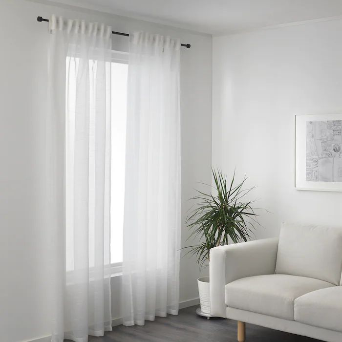 a living room with white curtains and a potted plant on the floor next to it