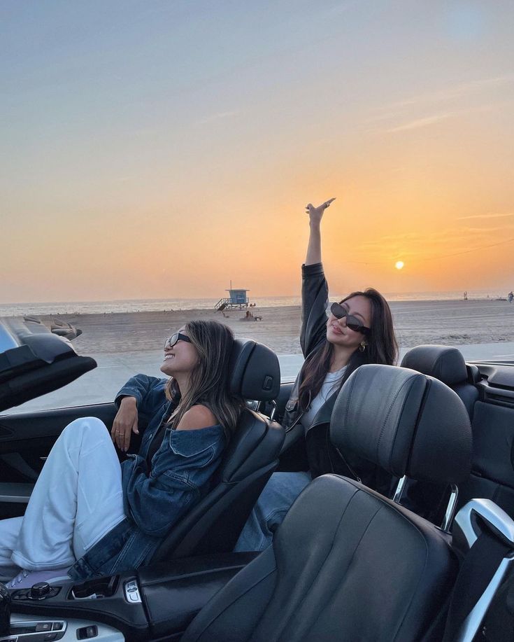 two women are sitting in the back of a car and one is raising her arms