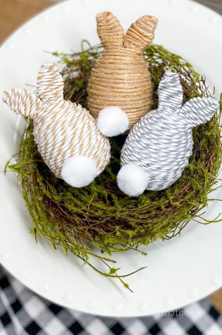 three small stuffed animals sitting on top of a white plate covered in grass and twine