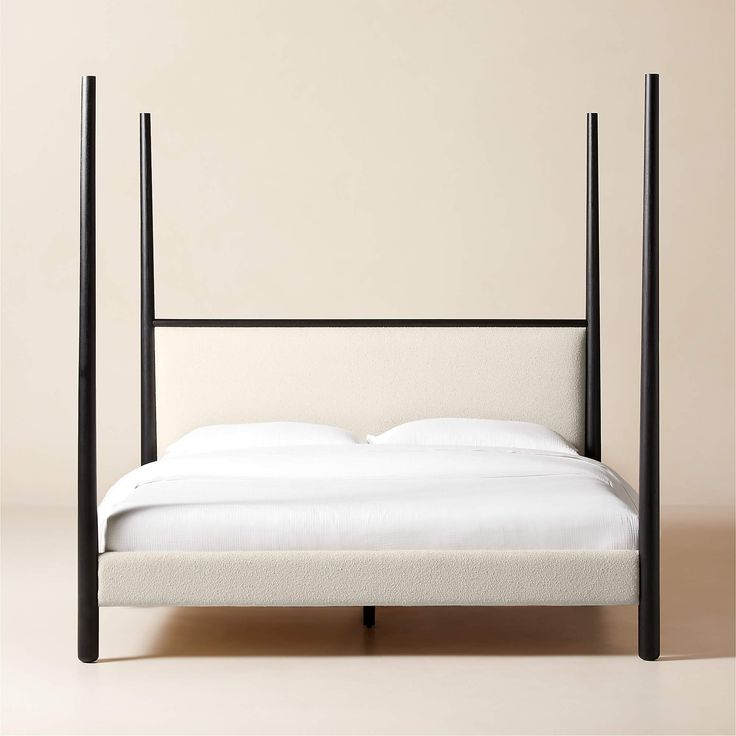 a bed with white sheets and black metal frame, in front of a beige wall