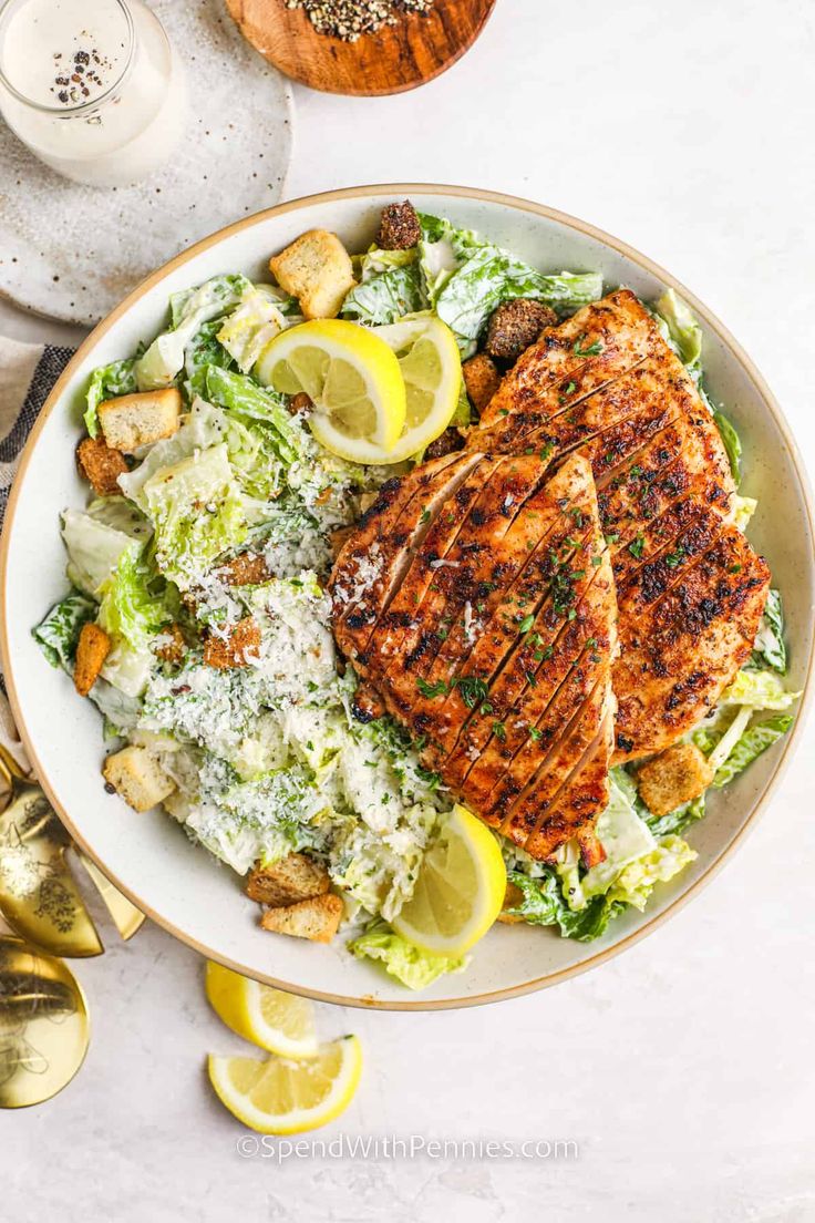 a white plate topped with chicken, lettuce and lemon wedges next to silverware