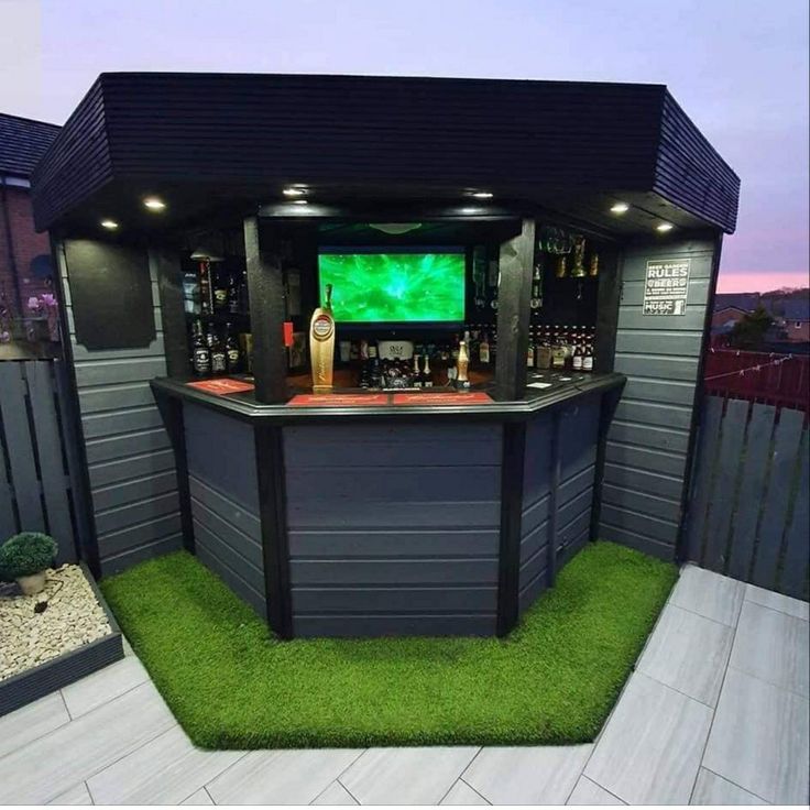 an outdoor bar with artificial grass and lights on the outside, in front of a fence