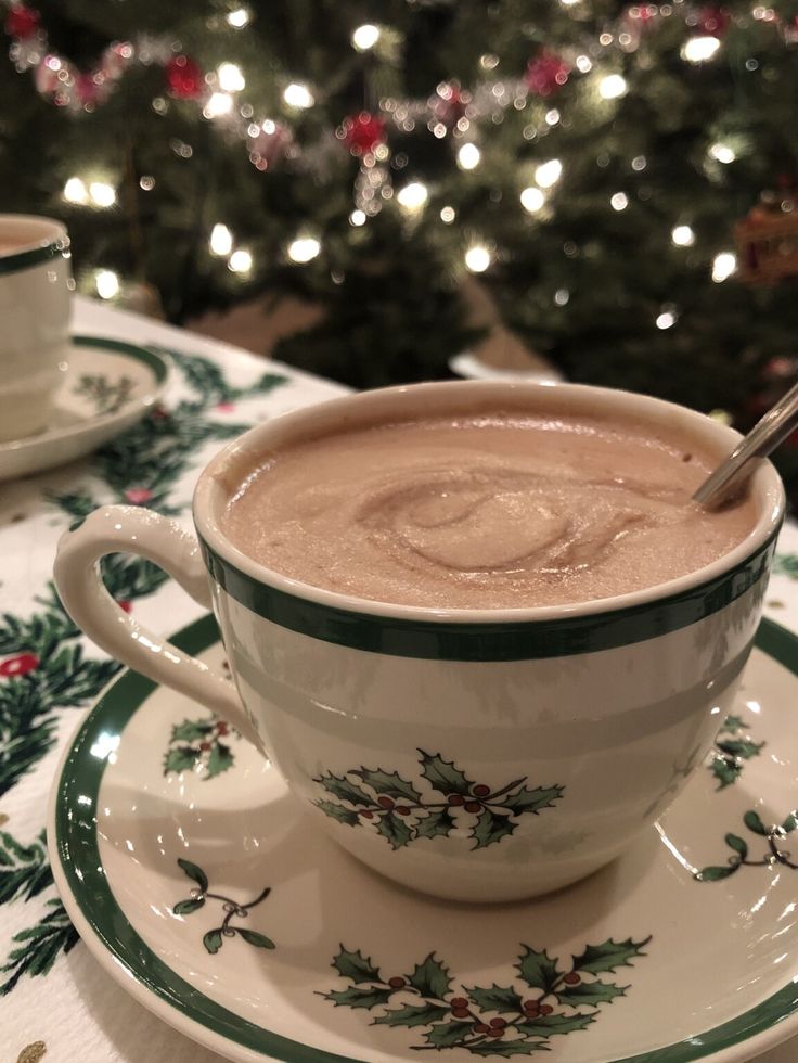 a cup of hot chocolate sitting on top of a saucer next to a christmas tree