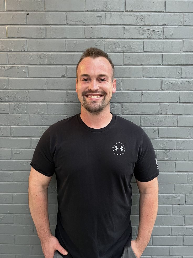 a man standing in front of a gray brick wall with his hands on his hips