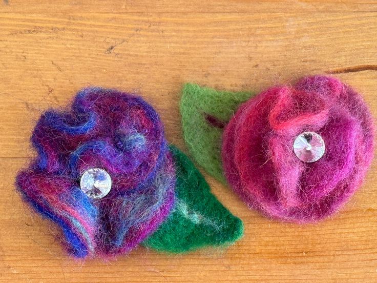 two felt flowers sitting on top of a wooden table