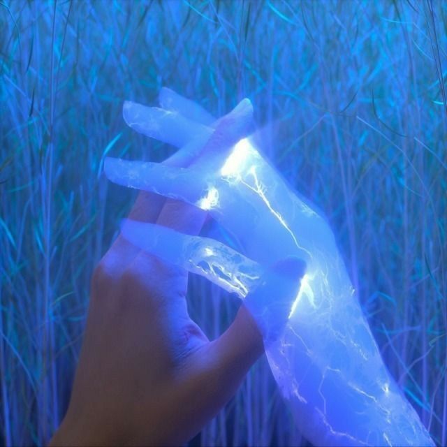 a hand holding an ice block in front of some tall grass with blue lights on it