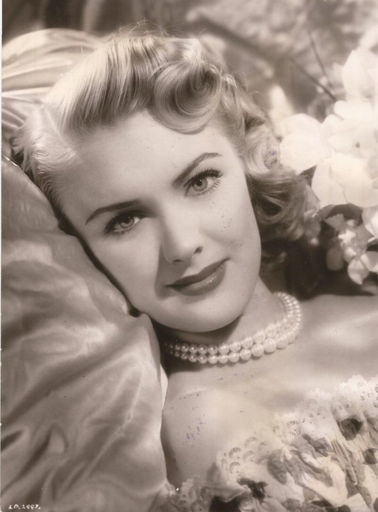 an old black and white photo of a woman with pearls on her neck laying down