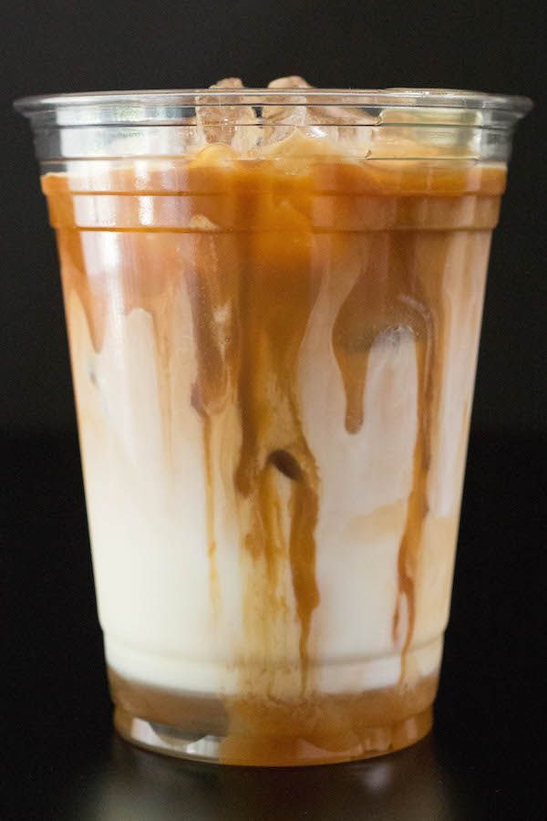 an iced drink in a plastic cup with ice and caramel on the top, sitting on a black surface