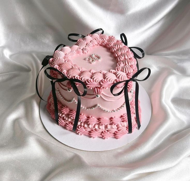 a heart shaped pink cake sitting on top of a white plate with black ribbon around it