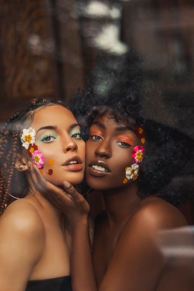 two beautiful women with flower decorations on their faces posing for the camera, both looking in opposite directions