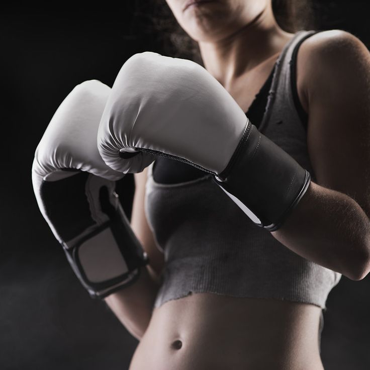 a woman wearing boxing gloves and holding a cell phone in her hand while standing against a dark background