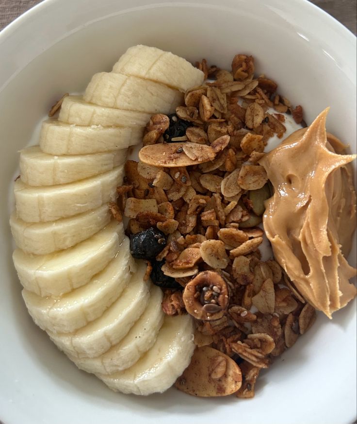 a white bowl filled with granola, bananas and nuts