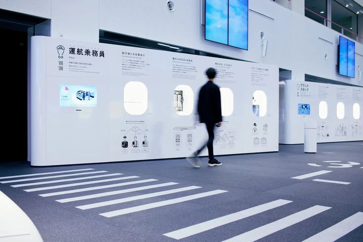 a man walking through an airport terminal next to white walls with information on them and windows