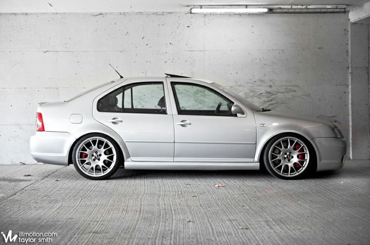 a silver car is parked in an empty space with concrete walls and flooring behind it