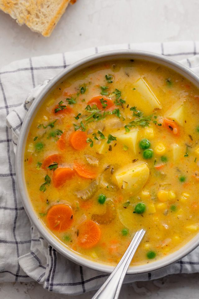 a bowl of soup with carrots, peas and bread on a towel next to it