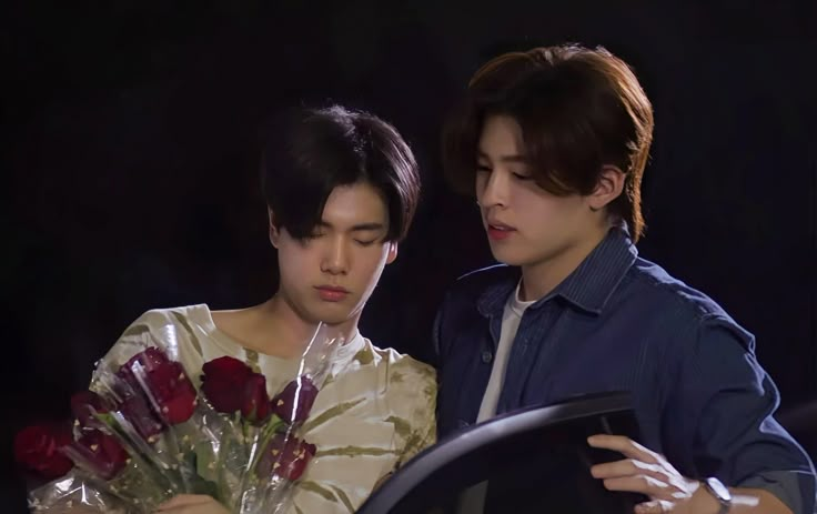 two young men standing next to each other holding flowers and looking at something in front of them