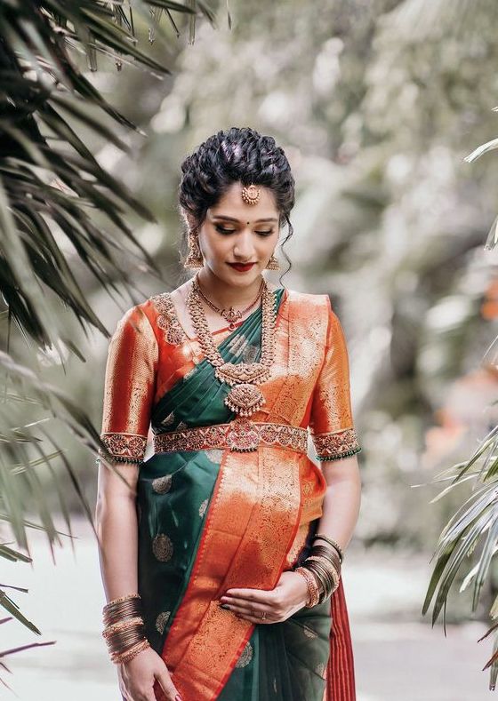 a woman in an orange and green sari standing next to some palm tree branches