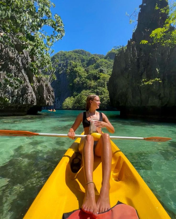 a woman in a yellow kayak paddling through the clear blue water near cliffs