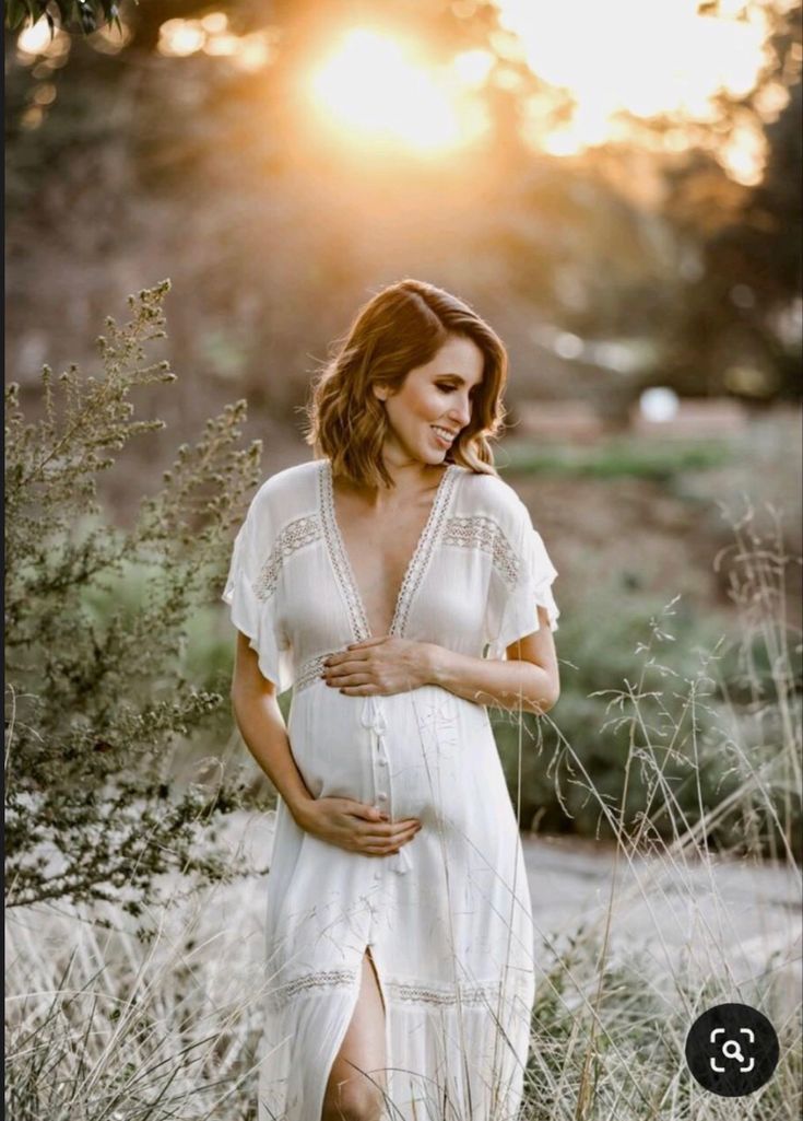 a pregnant woman standing in tall grass at sunset