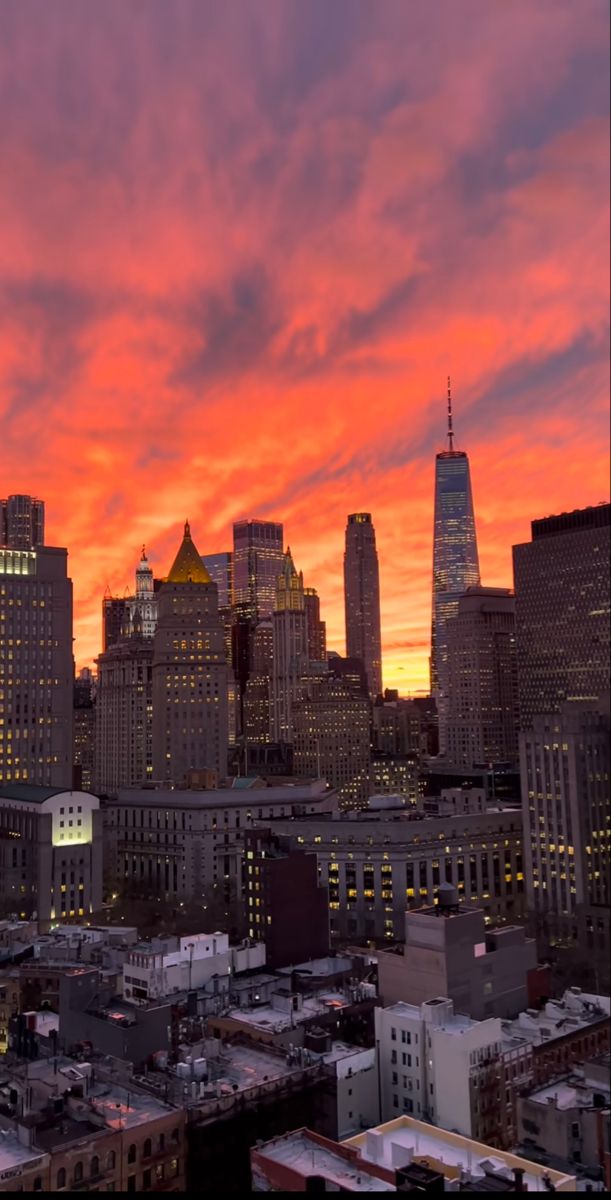 the city skyline is lit up at night with bright orange and pink clouds in the sky