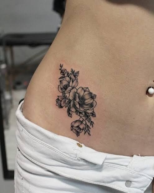 a woman's lower back tattoo with flowers on her left side ribcage