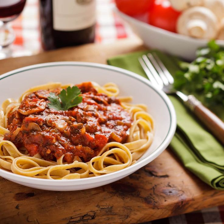 a white bowl filled with pasta and sauce on top of a wooden cutting board next to a bottle of wine