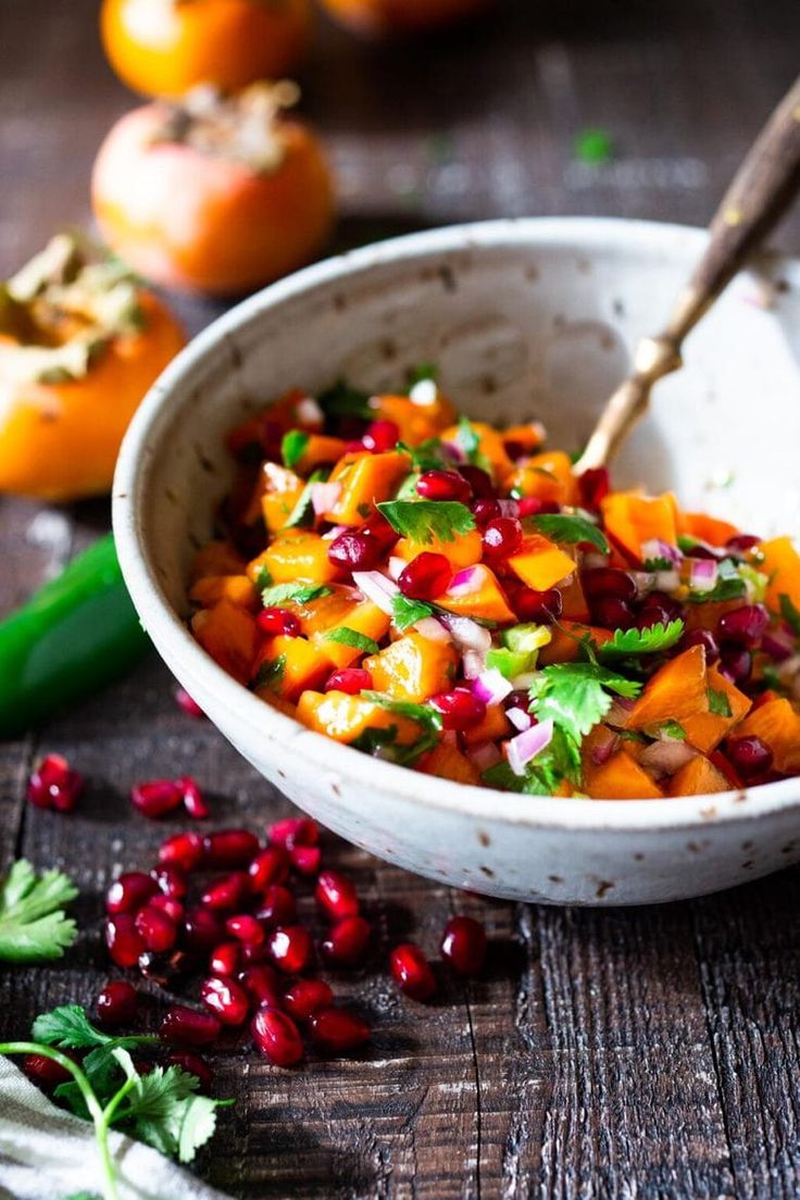 a bowl filled with fruit and vegetables on top of a wooden table next to pomegranates