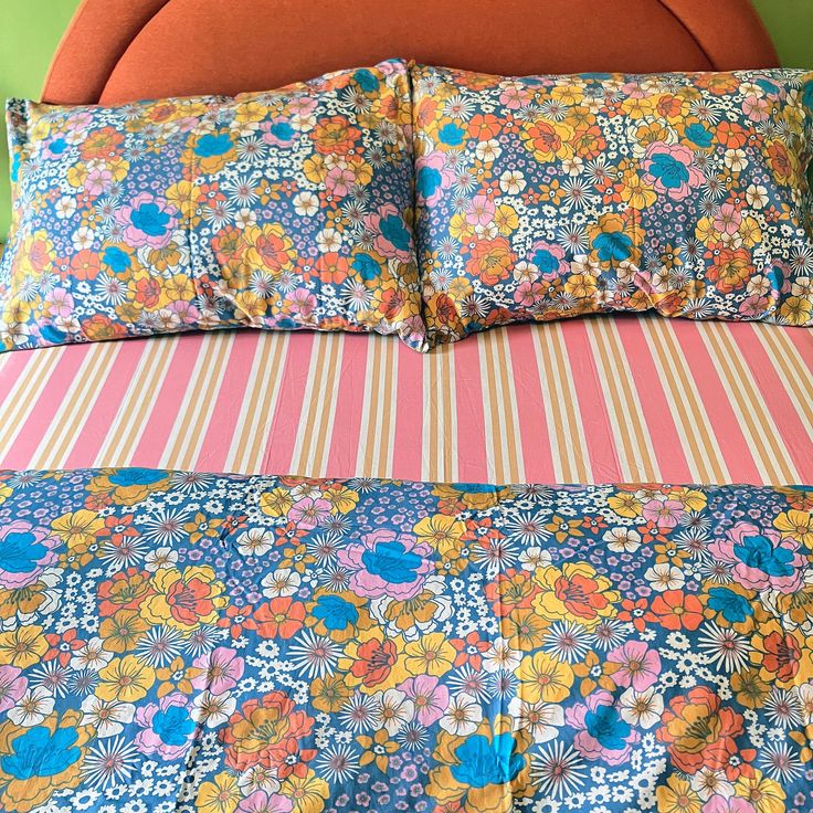 an orange headboard is next to a bed with colorful floral sheets and pillow cases