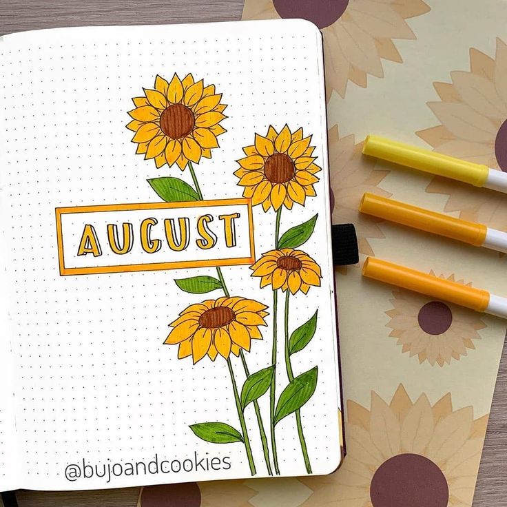 an open notebook with sunflowers on it next to two markers and pencils