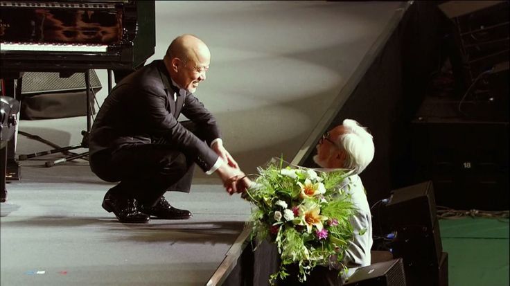 an older man is giving flowers to a younger woman in front of a stage set