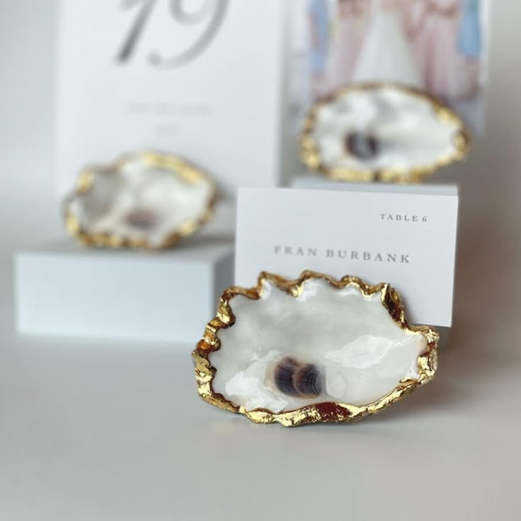 two small white and gold dishes sitting on top of a table next to a card