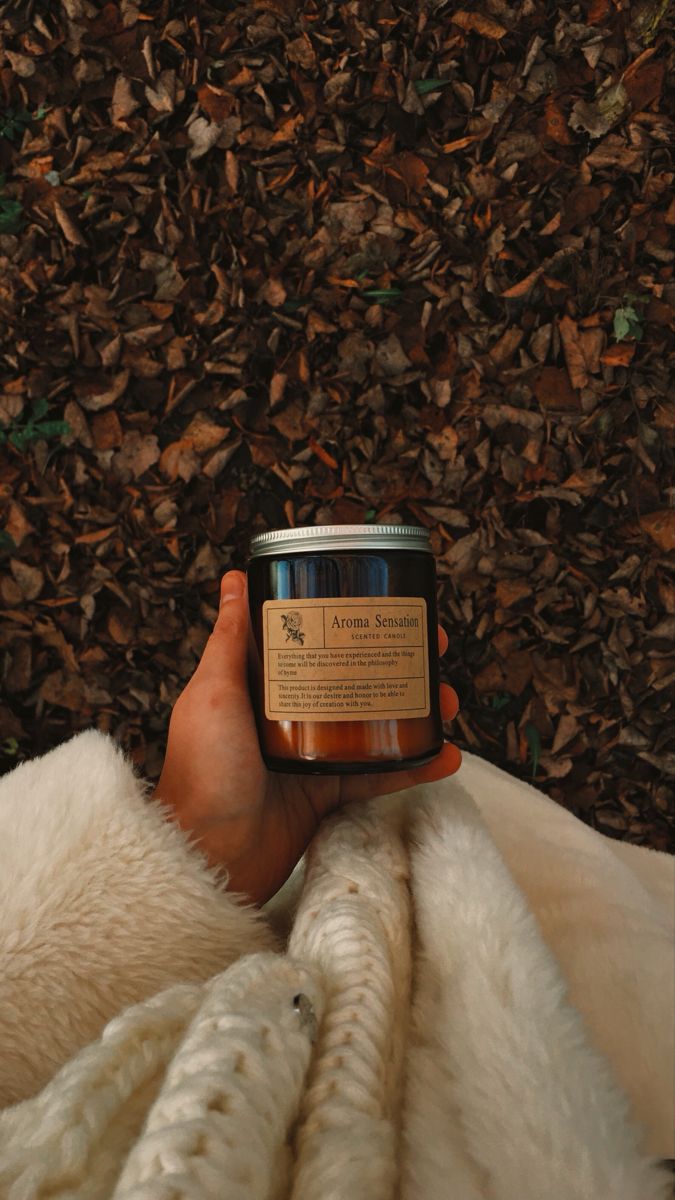 a person holding a candle in their hand while laying on the ground covered with leaves