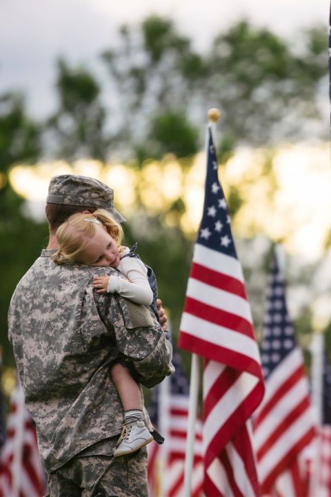 a soldier holding a small child in his arms next to american flags and an american flag