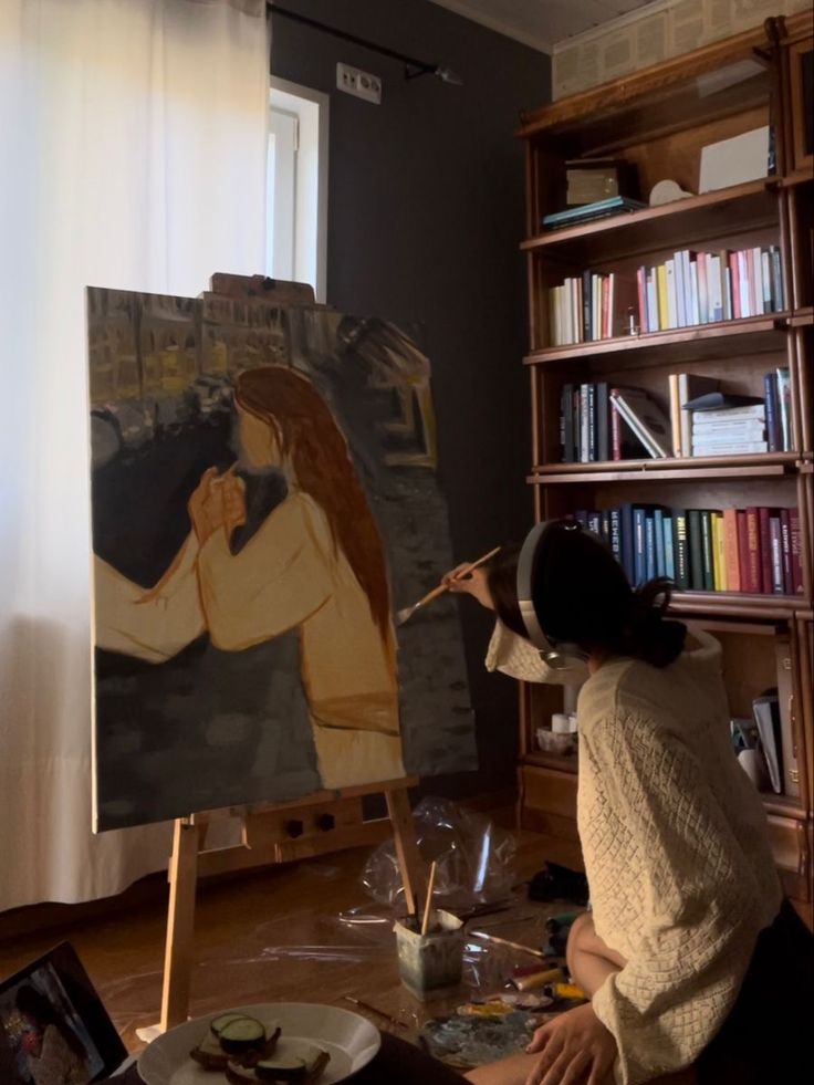 a woman sitting on the floor in front of an easel with a painting on it