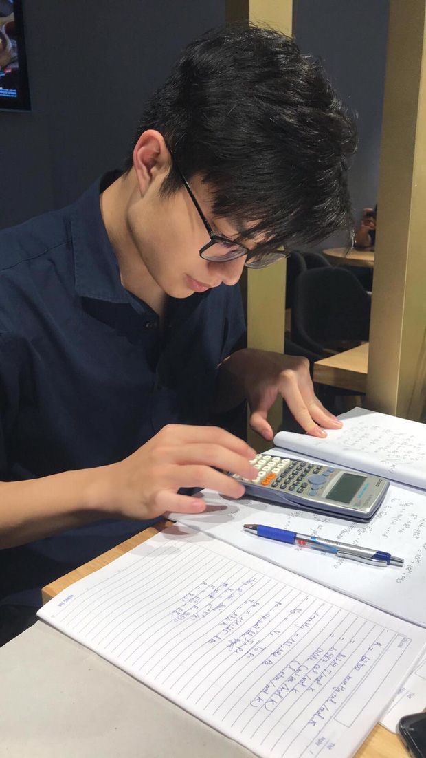 a young man sitting at a desk using a calculator and writing on a piece of paper