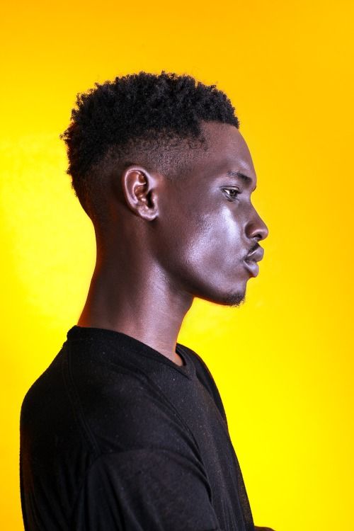 a man with black paint on his face standing in front of a yellow background and looking off to the side