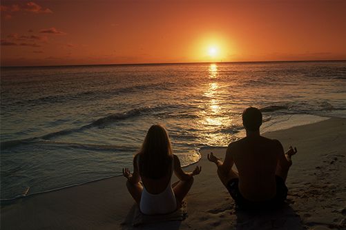 two people sitting on the beach at sunset