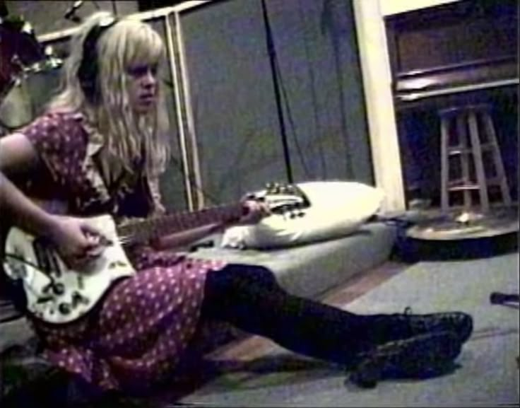 a woman sitting on the floor playing an electric guitar