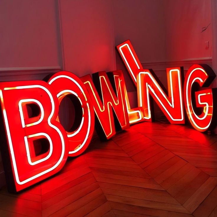 the word bowling is lit up in red and white neon letters on a wooden floor