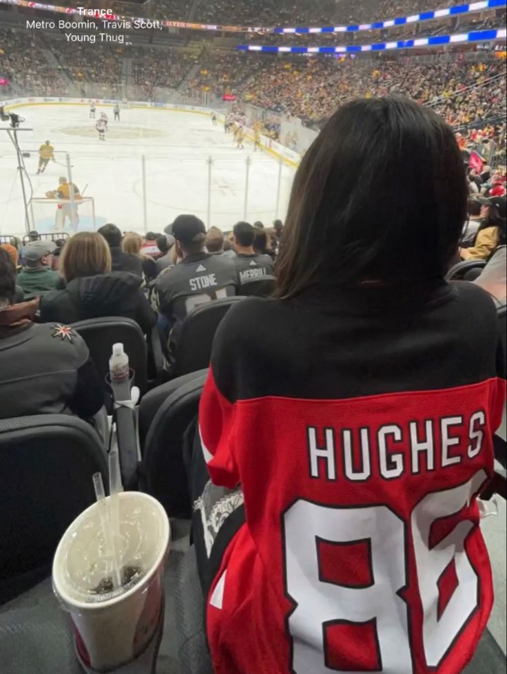 a hockey fan is sitting in the stands at an ice rink with her jersey draped over her shoulders