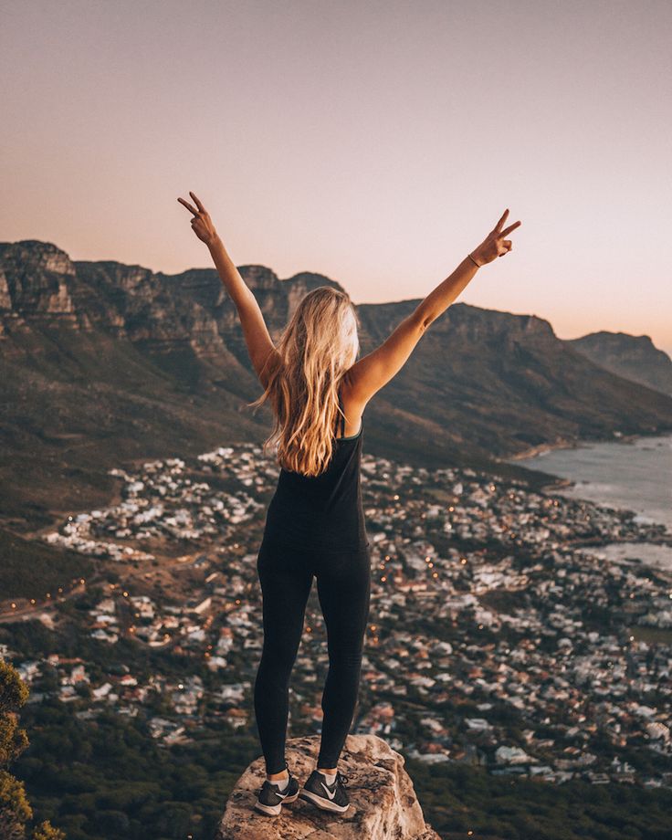 a woman standing on top of a cliff with her arms outstretched