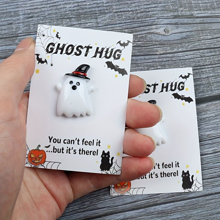 a hand holding two halloween ghost magnets on top of a wooden table next to each other