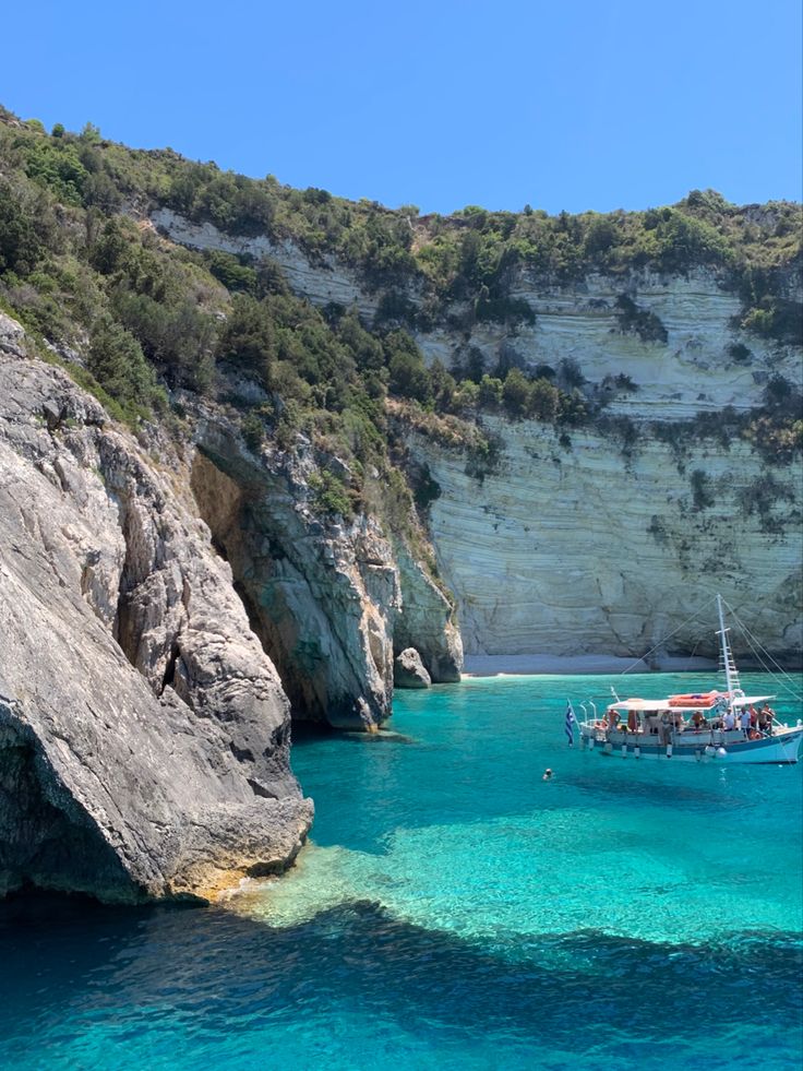 a boat is in the clear blue water near some rocks and cliffs on a sunny day