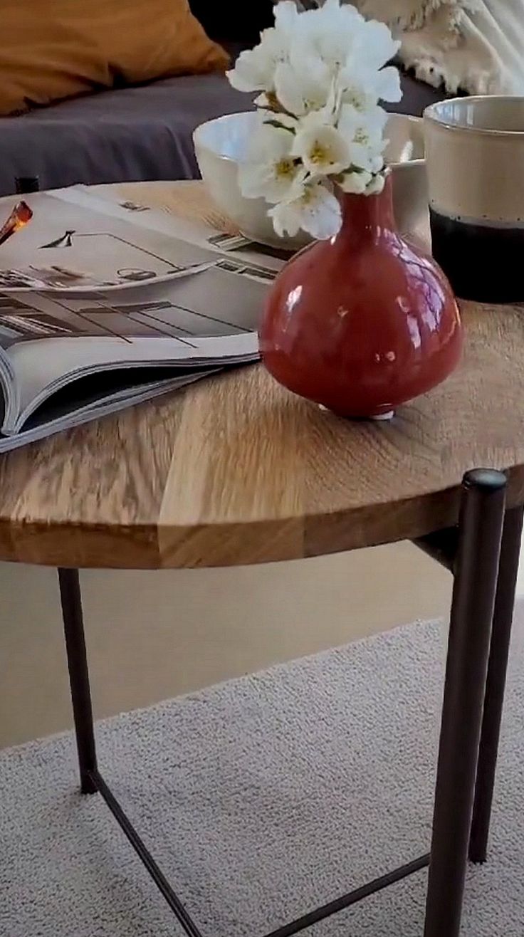 a table with magazines and flowers on it in front of a couch, coffee table