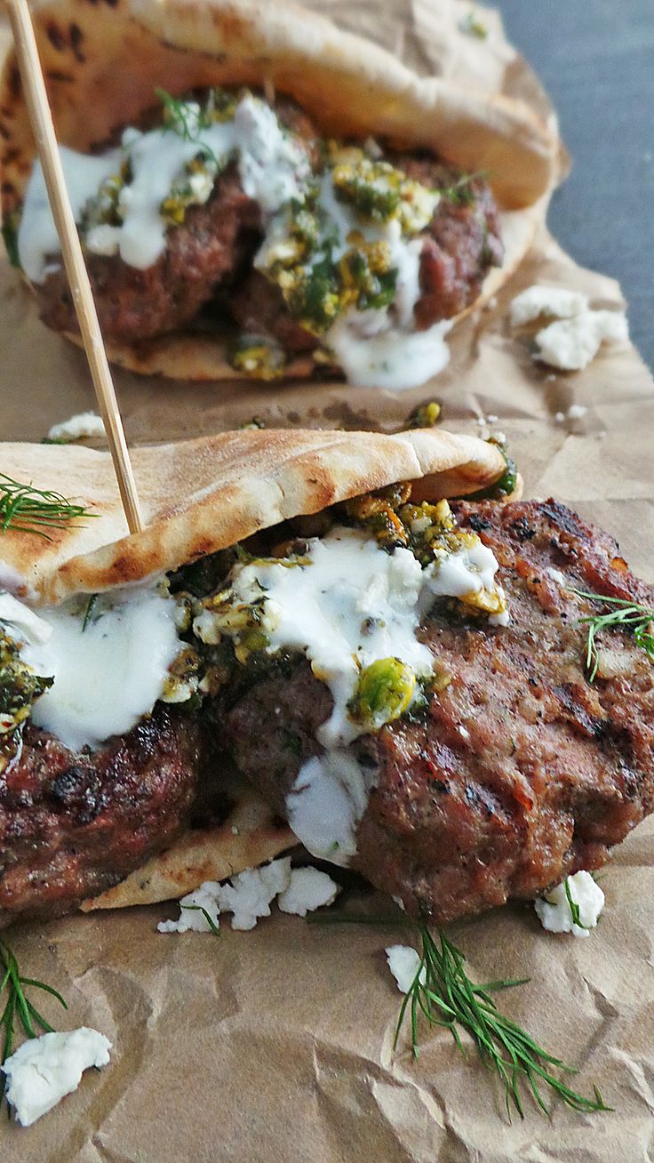 two meat patties with white sauce and herbs on top, sitting on wax paper